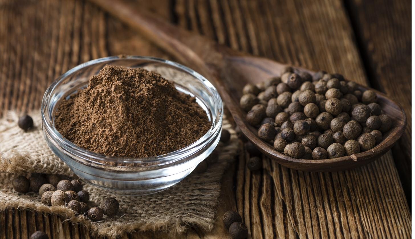 Ground allspice and whole berries in a wooden bowl and spoon on a rustic table