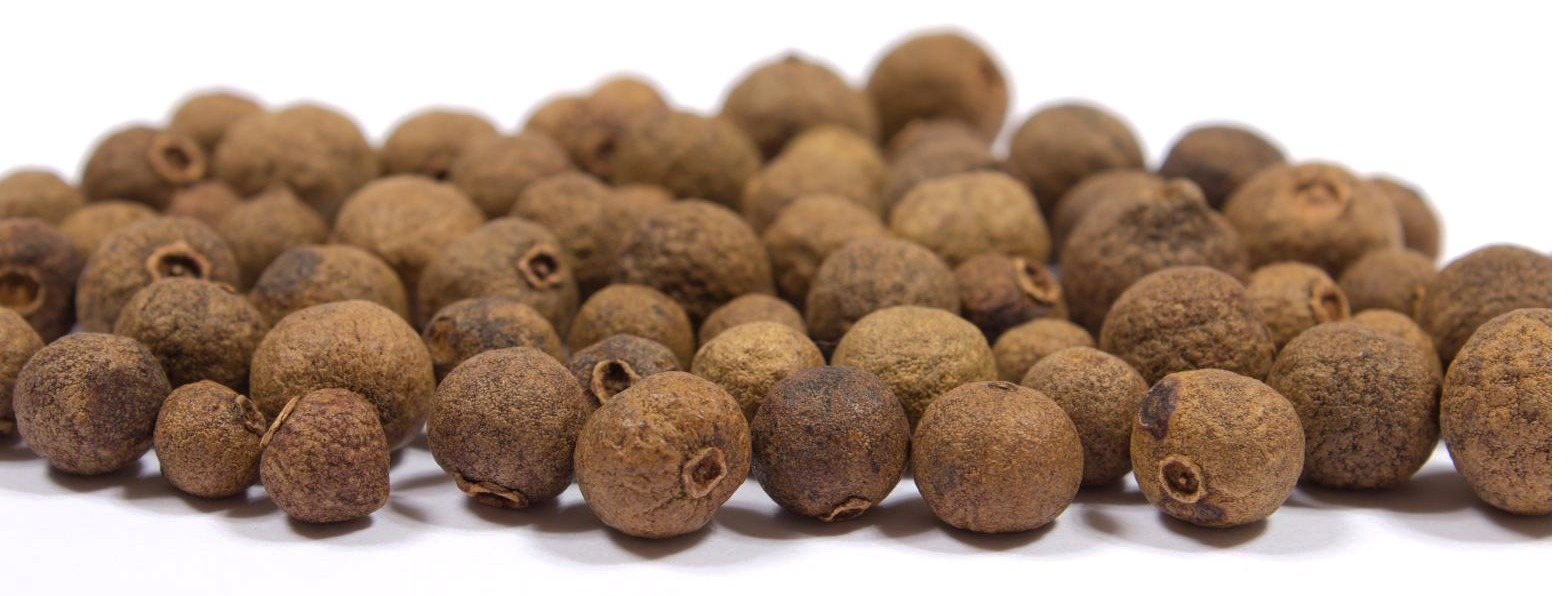 Whole allspice berries in a loose heap on a white surface