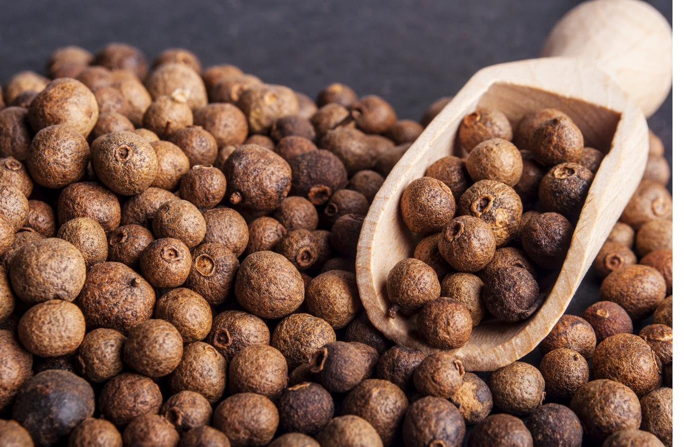 Whole allspice berries heaped beside a wooden scoop