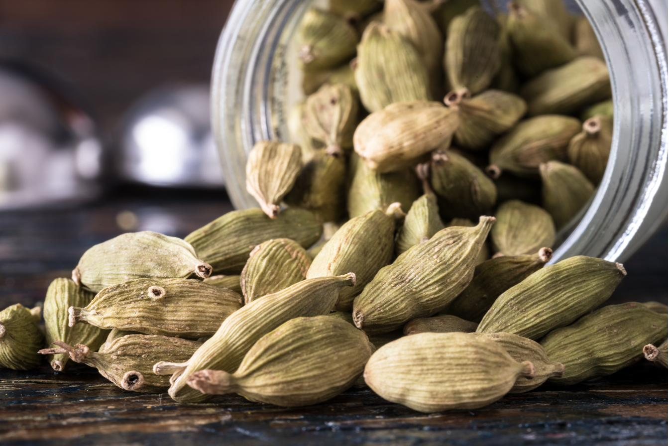 Green cardamom pods spilling from a tipped glass jar