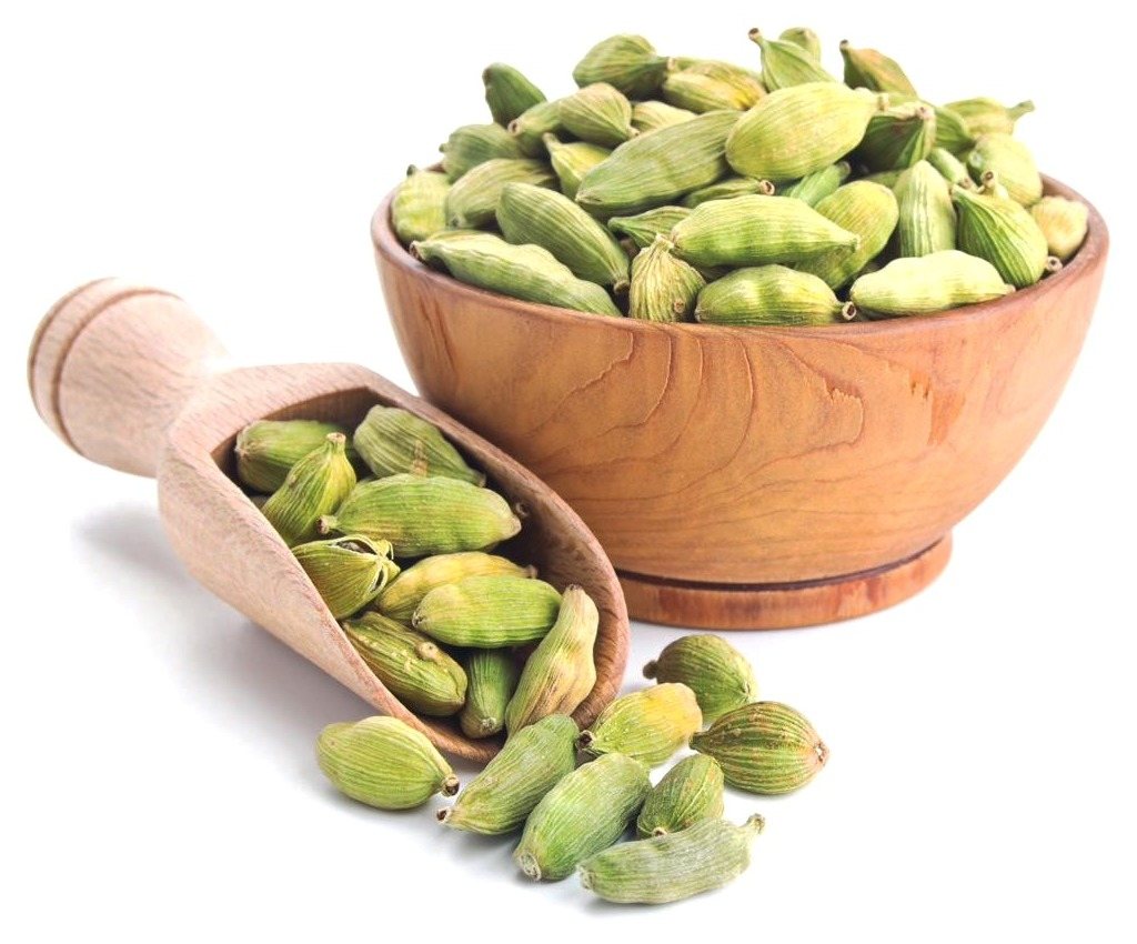 Green cardamom pods in a wooden bowl and scoop, spilling onto a white surface