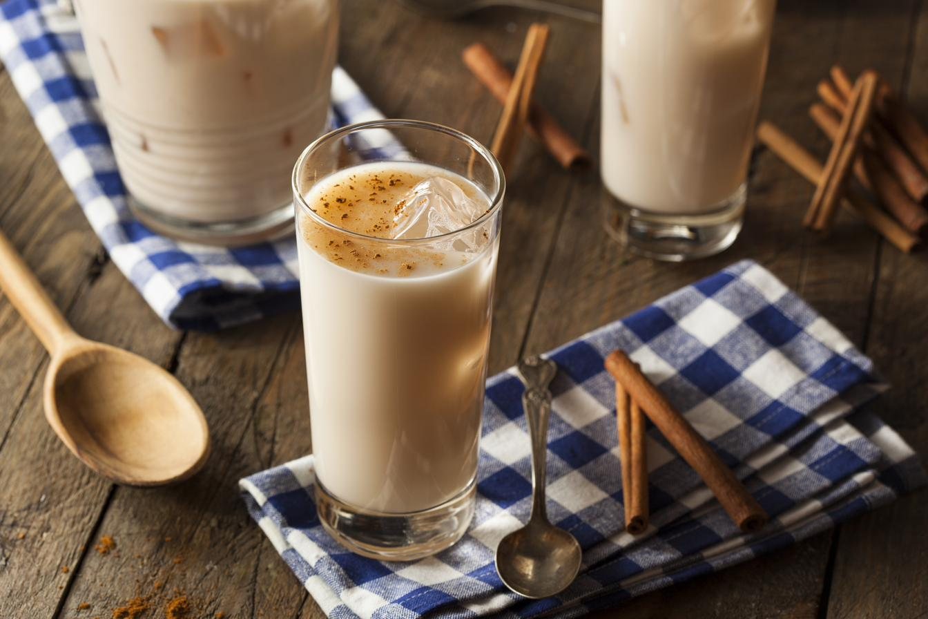 Glasses of a creamy spiced drink garnished with cinnamon sticks on a checked cloth