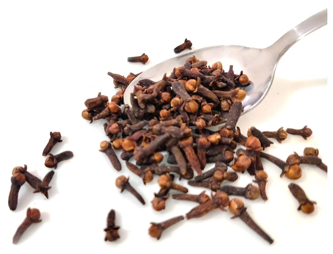 A spoonful of whole cloves, with more scattered across a white surface