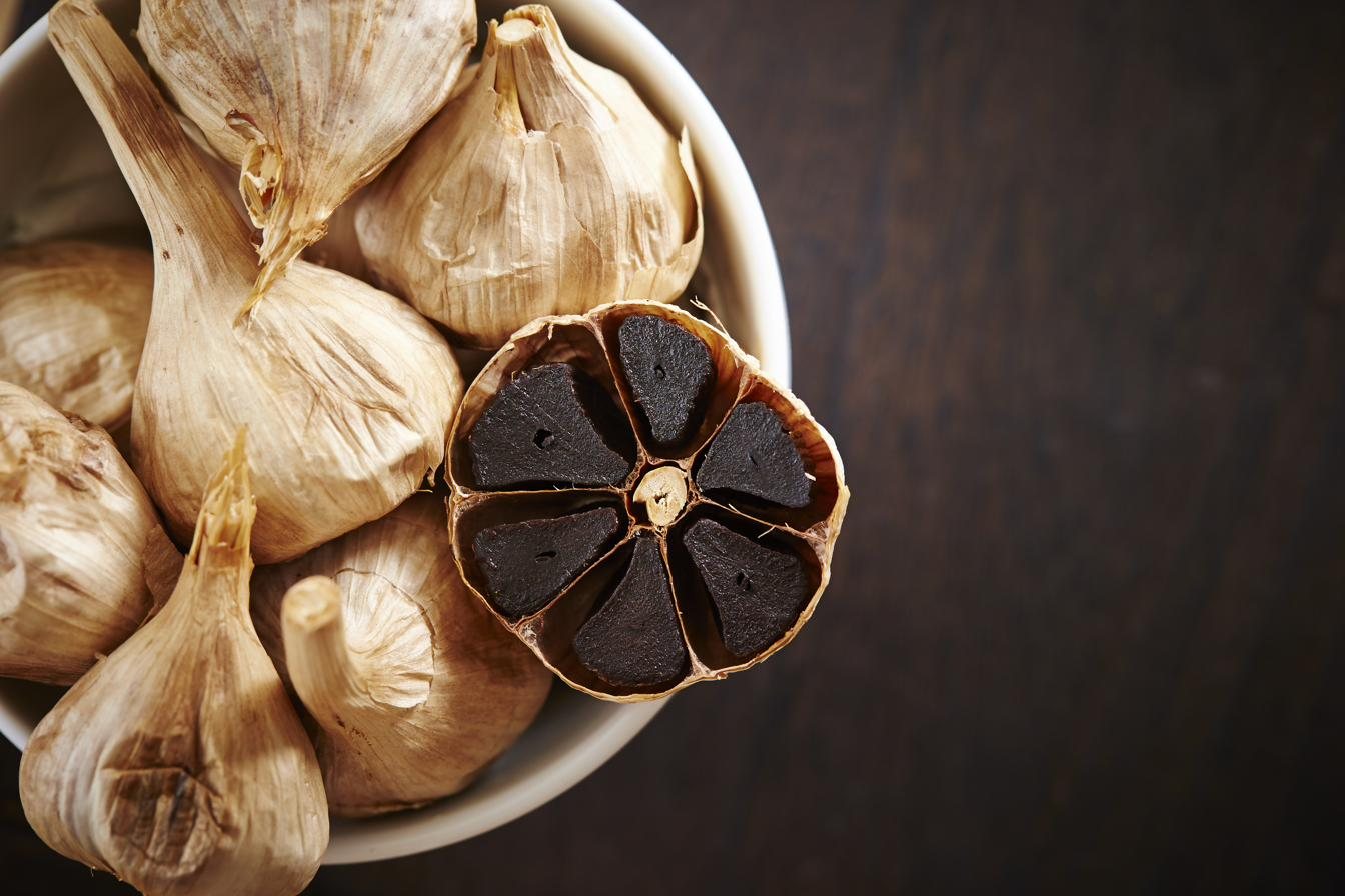 Whole and halved heads of black garlic in a bowl