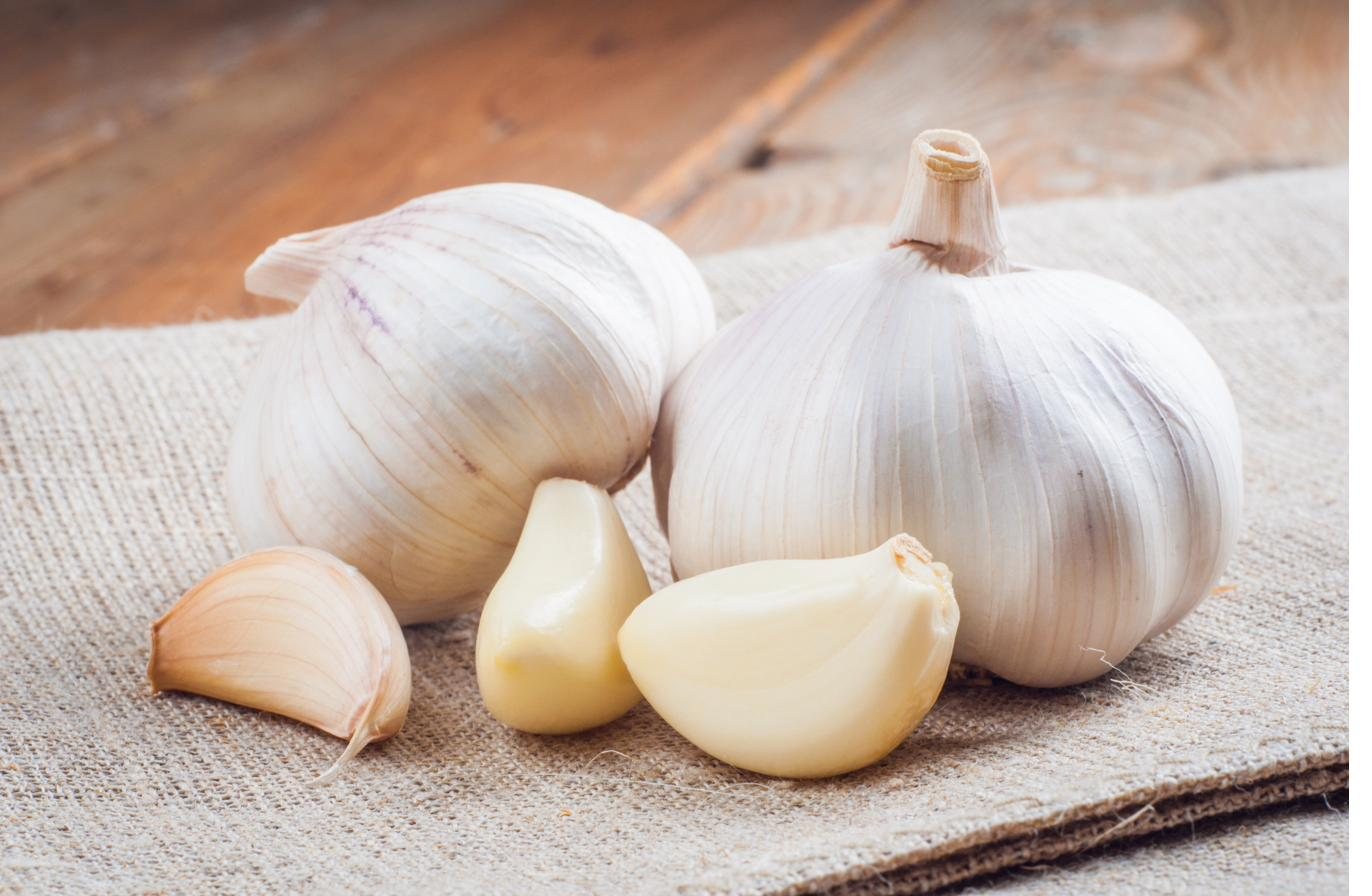 Two garlic heads and a few loose cloves on a burlap cloth