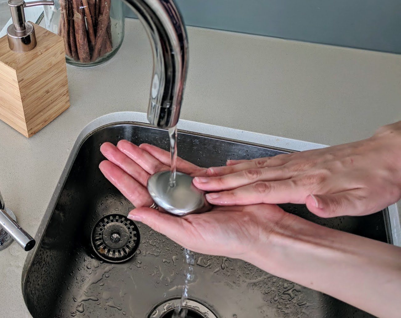 Hands rubbing a stainless steel soap bar under a running kitchen faucet