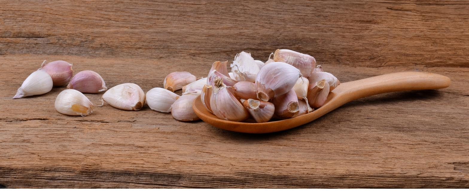 Garlic cloves heaped in a wooden spoon, with more scattered across a weathered wooden table