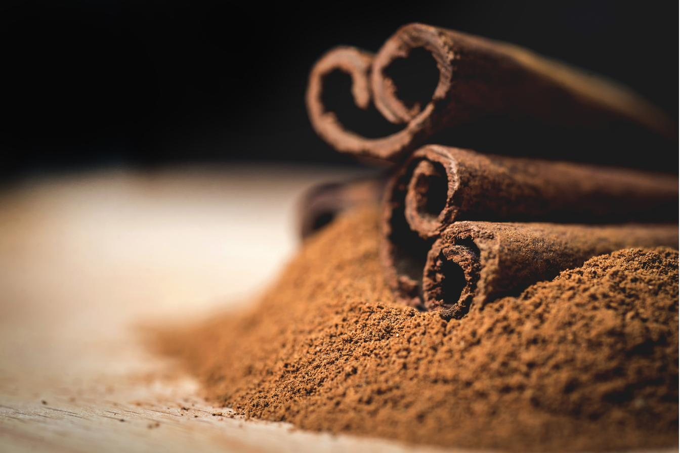 Cinnamon sticks resting on a mound of ground cinnamon against a dark background