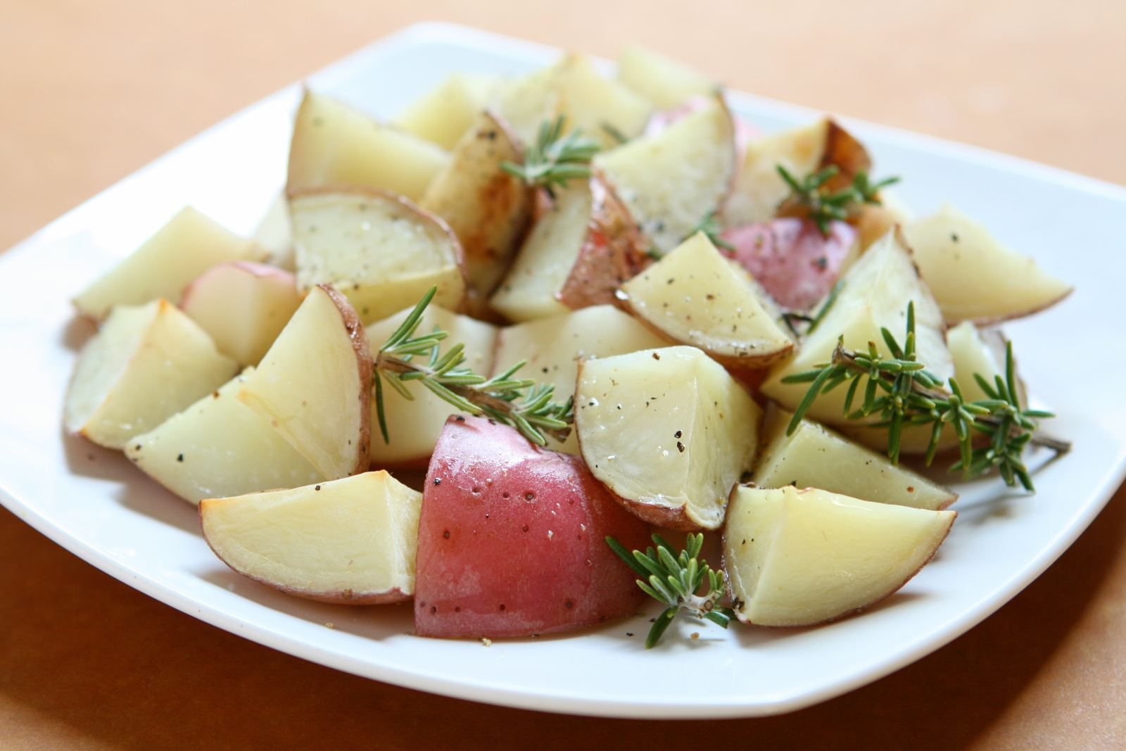Roasted red potato wedges with rosemary sprigs on a white plate