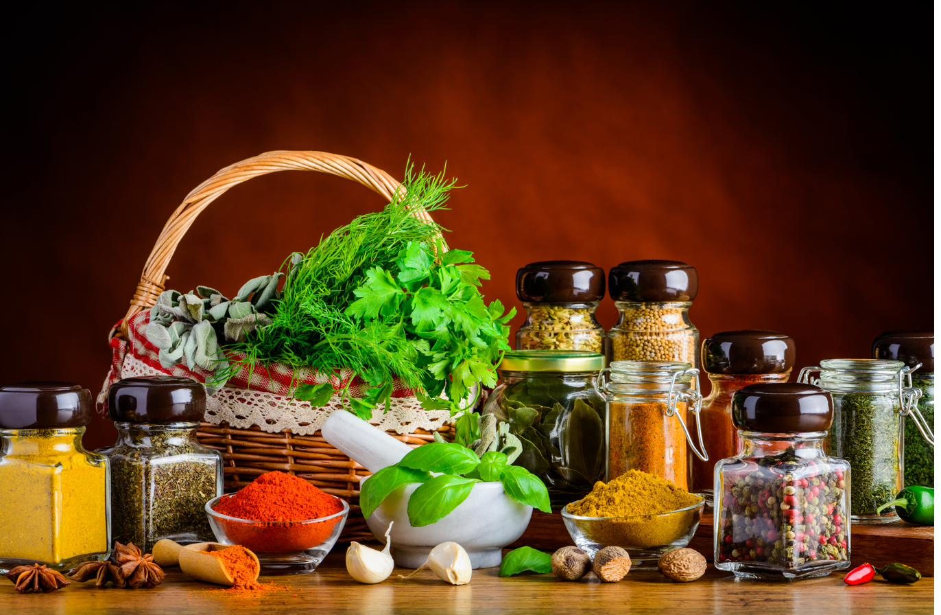 A basket of fresh herbs surrounded by jars of dried spices