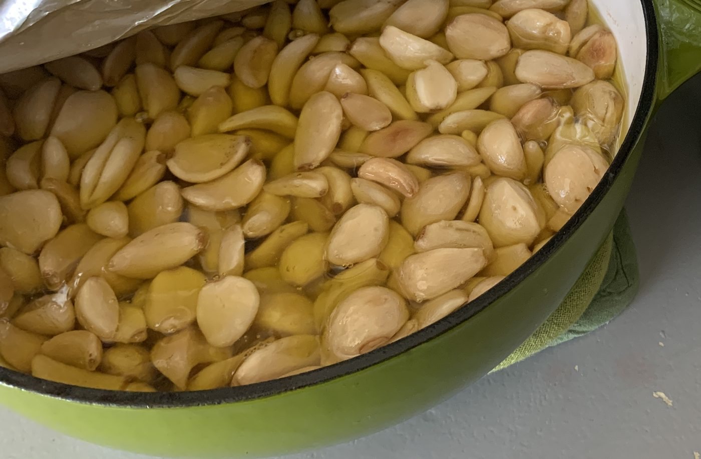 Peeled garlic cloves cooking slowly in olive oil in a green pot