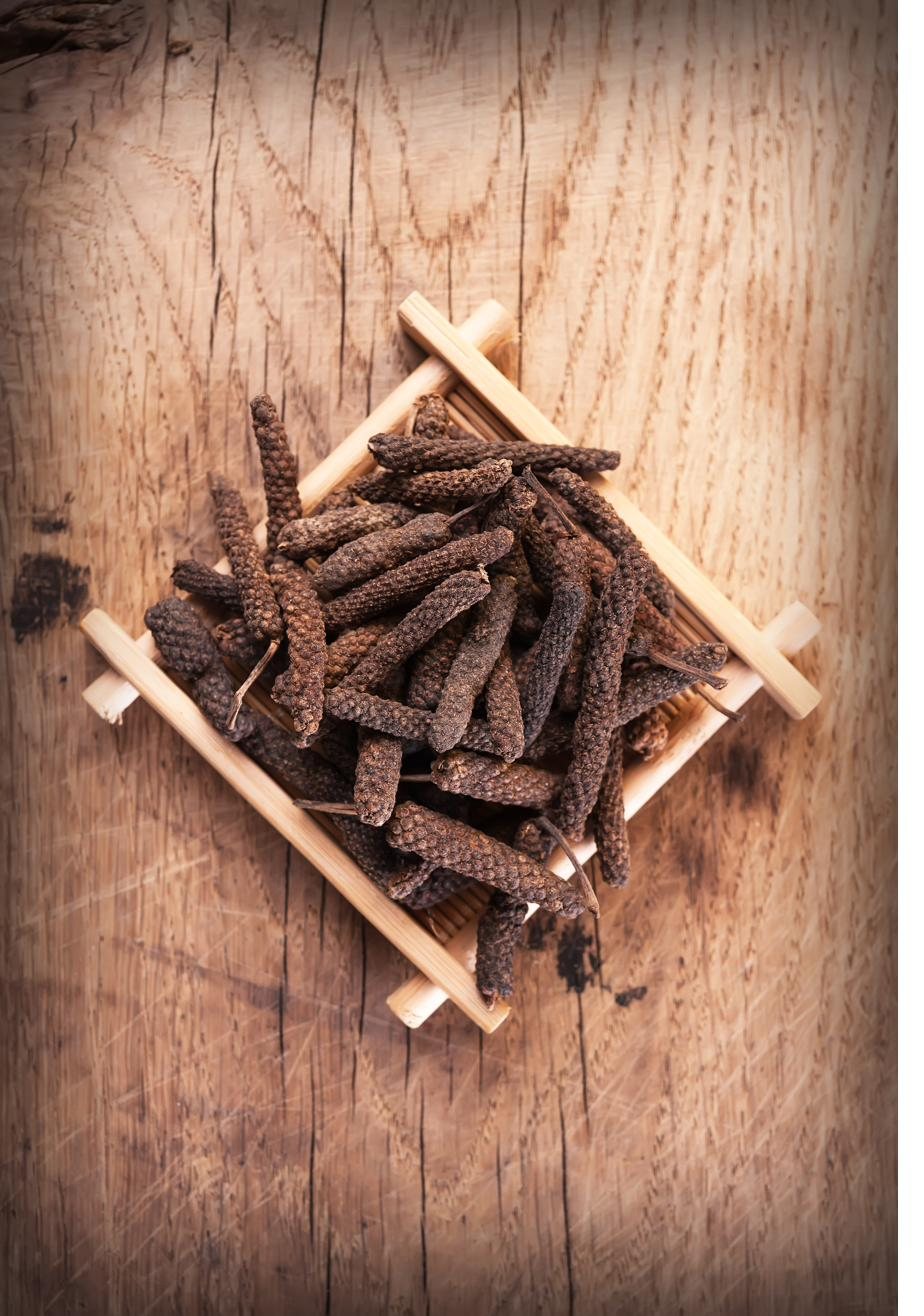 Long pepper catkins arranged inside a small frame of wooden sticks on a rustic table