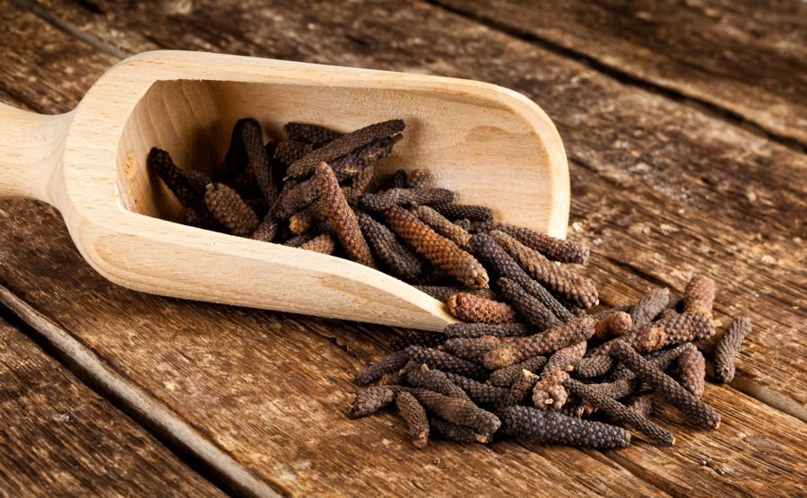 Long pepper catkins spilling from a wooden scoop onto a table