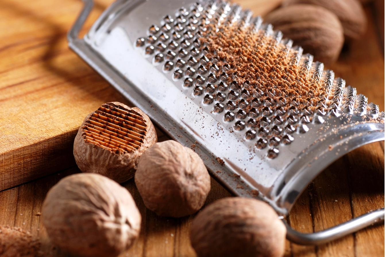 Whole nutmegs beside a metal grater dusted with freshly grated nutmeg
