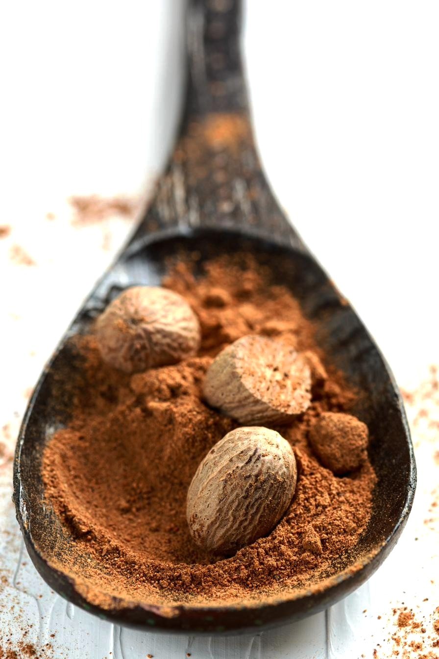 Whole nutmegs resting in a dark wooden spoon of ground nutmeg