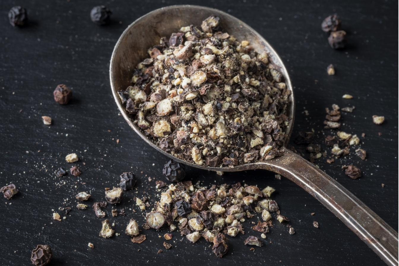 Freshly cracked black pepper heaped in a vintage spoon on dark slate