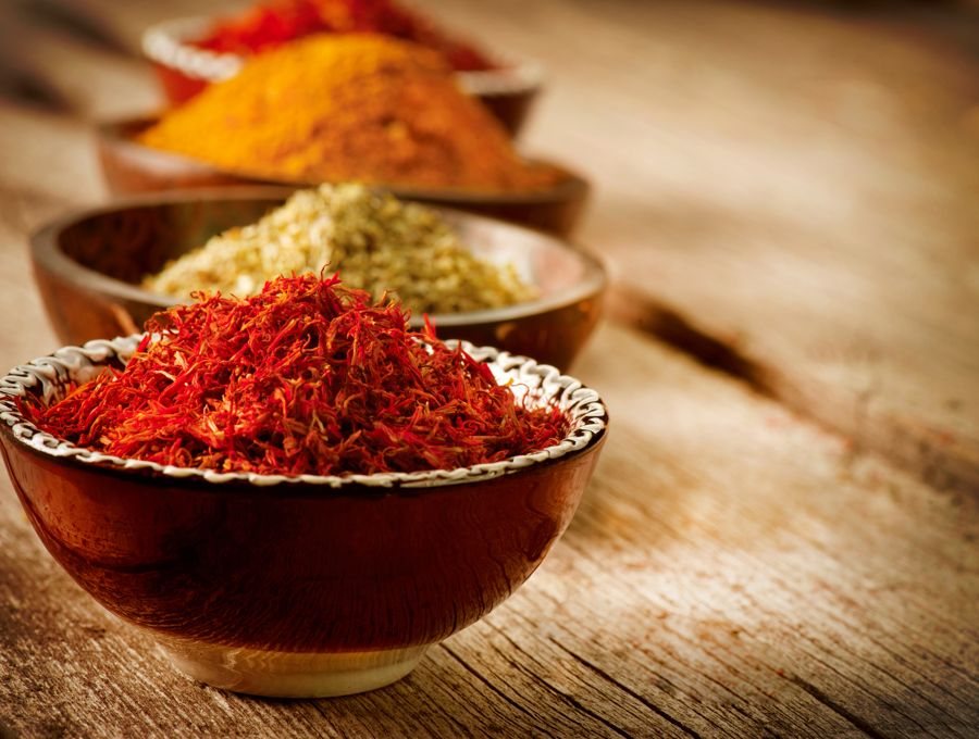 A bowl heaped with saffron threads in front of bowls of ground spices