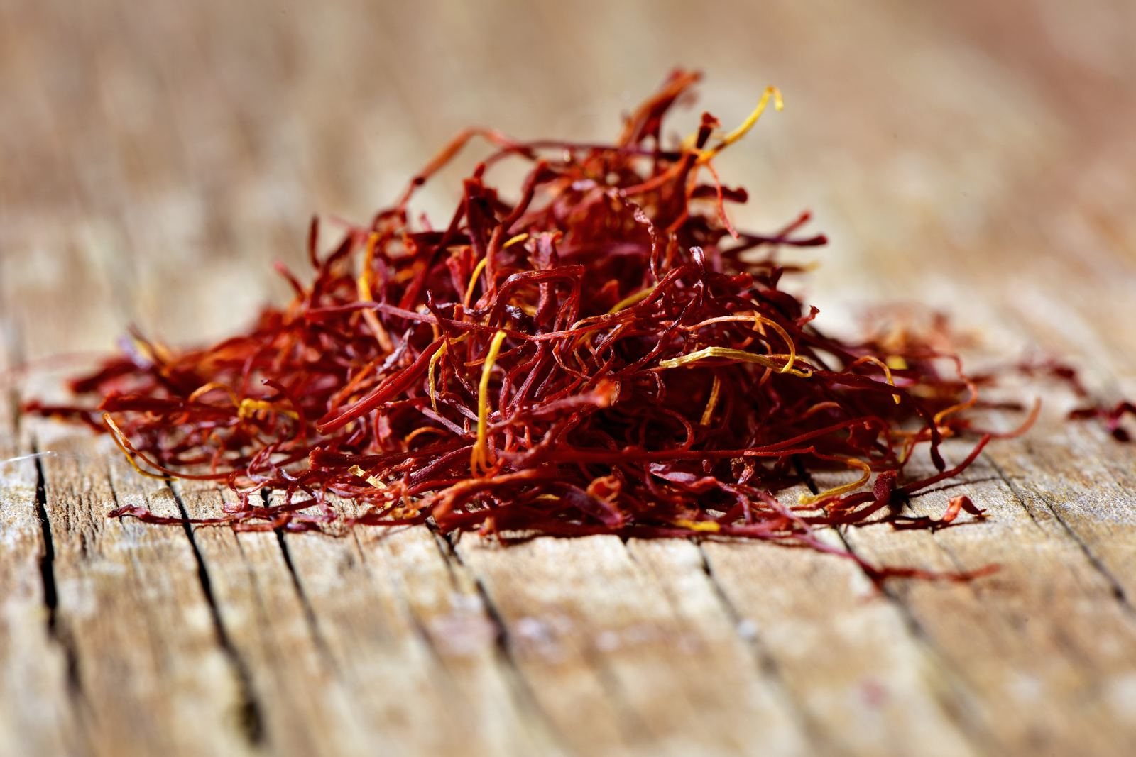 A loose pile of deep red saffron threads on weathered wood
