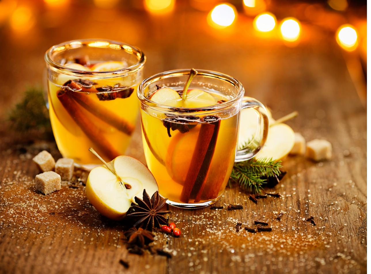 Two glass mugs of hot spiced wassail with apple slices, cinnamon sticks, and star anise